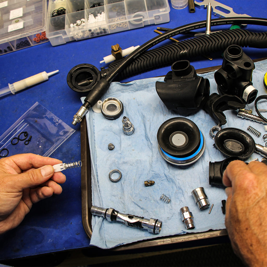 A student is holding two pieces of a broken down regulator. Under their hands is an array of other pieces. 